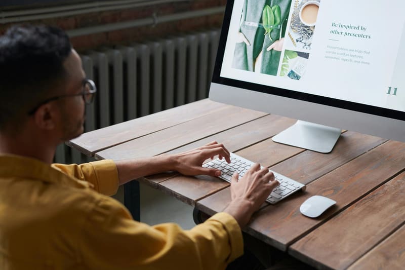 A student in a yellow shirt typing at a desktop computer on a wooden desk